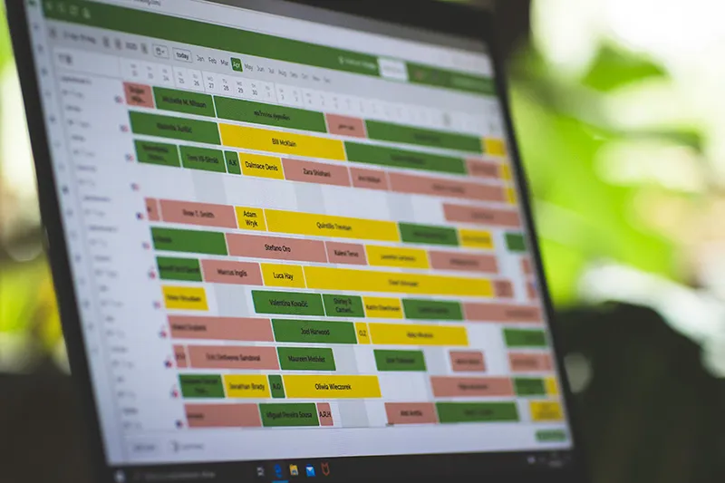 Ekran laptopa z kalendarzem rezerwacji z kolorowymi blokami w zielonym, żółtym i różowym