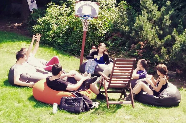 Osoby odpoczywające na pufach w ogrodzie przy koszu do koszykówki
