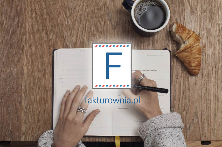 Otwarty notatnik, kawa i rogalik na drewnianym blacie z logo fakturownia.pl