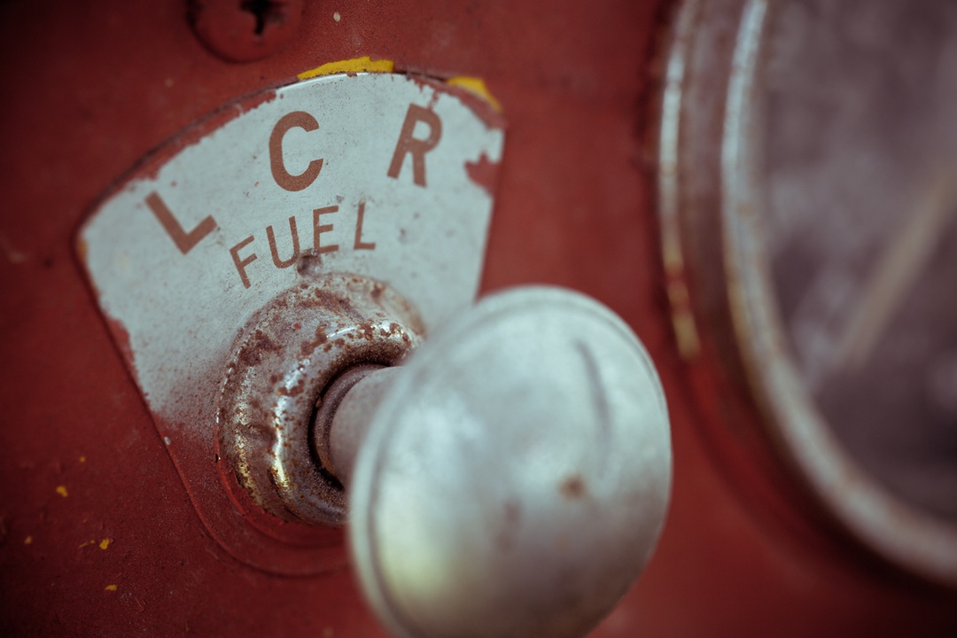 Zbliżenie na metalową gałkę z tabliczką L C R FUEL na czerwonej maszynie