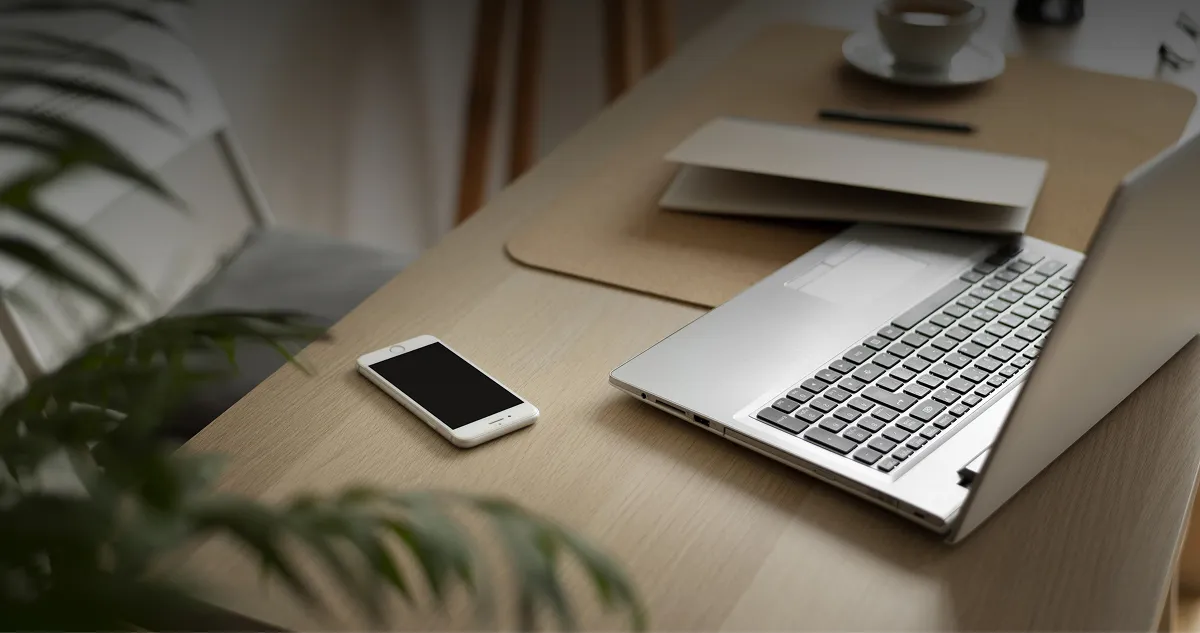 Laptop i smartfon na drewnianym biurku obok filiżanki kawy