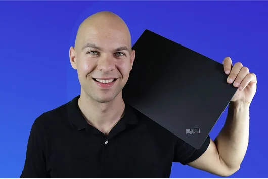 Krzysztof Gonet, właściciel NetGonet, trzymający laptopa ThinkPad na niebieskim tle