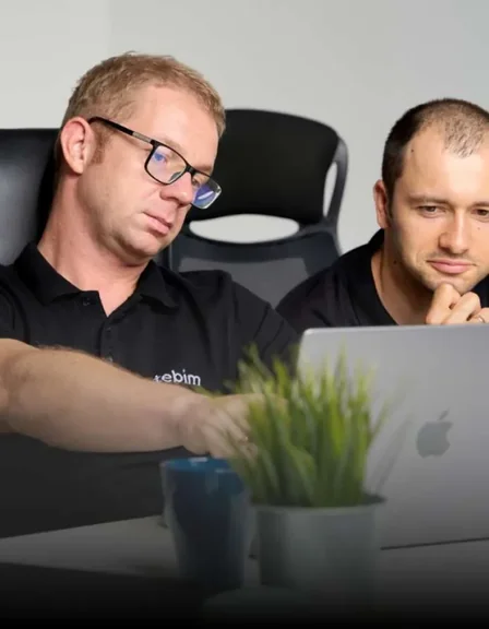 Dwóch mężczyzn w koszulkach z napisem Tebim przy laptopie Apple