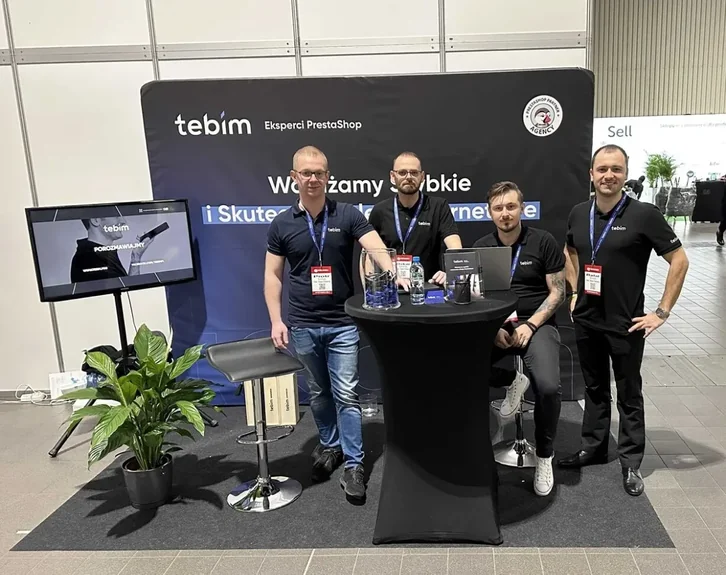 Czterech mężczyzn przy stoisku targowym z banerem Tebim – Eksperci PrestaShop